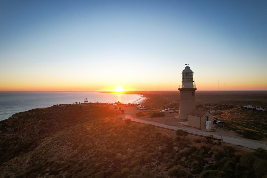 The sun sets behind a lighthouse.