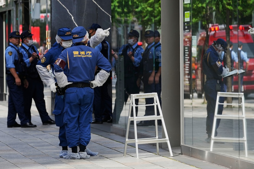 People in hazmat suits stand outside a building.