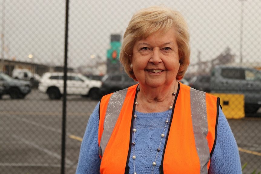 Maureen smiles while wearing a blue jumper and high vis orange vest.