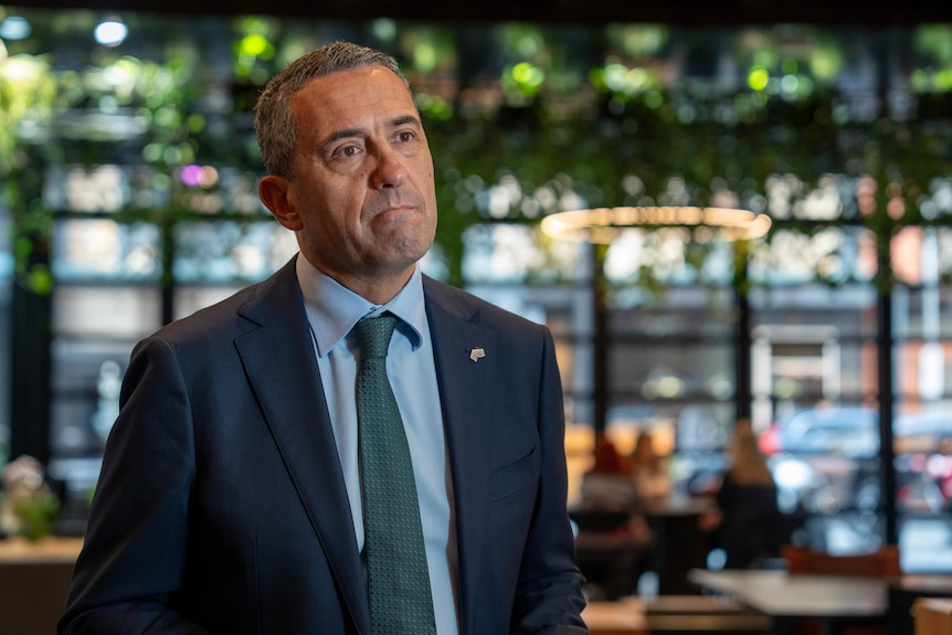 Tom Koutsantonis pursed lips in a serious expression in a room with large glass windows and  plants hung from the ceiling