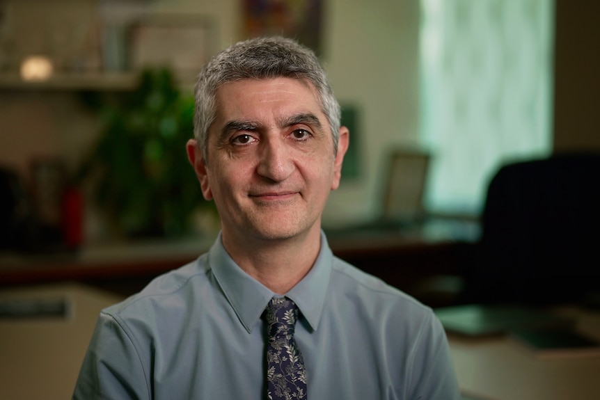 A man in a shirt and tie smiles at the camera.