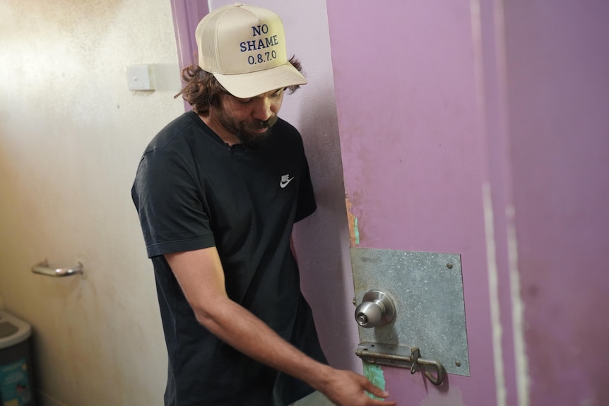 A young Aboriginal man displays a metal slide bolt on a purple door.