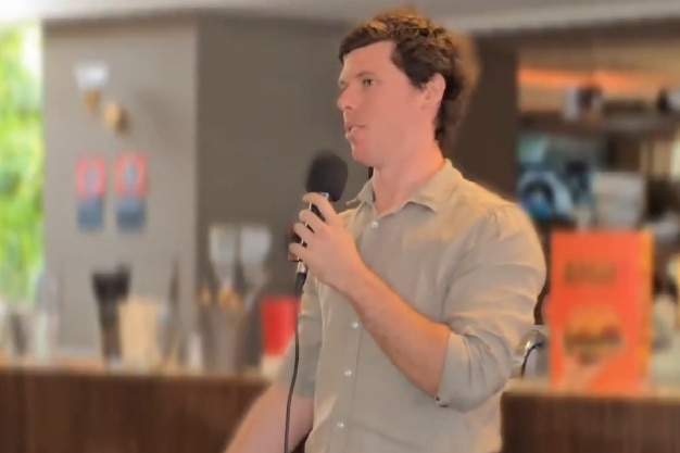 A man holding a microphone and wearing a beige shirt
