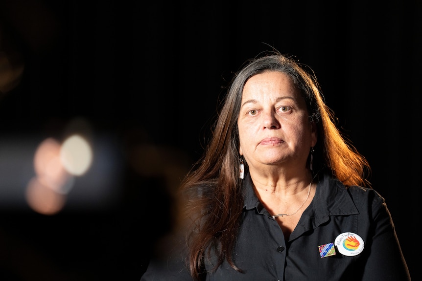 A woman being interviewed in a dark room.