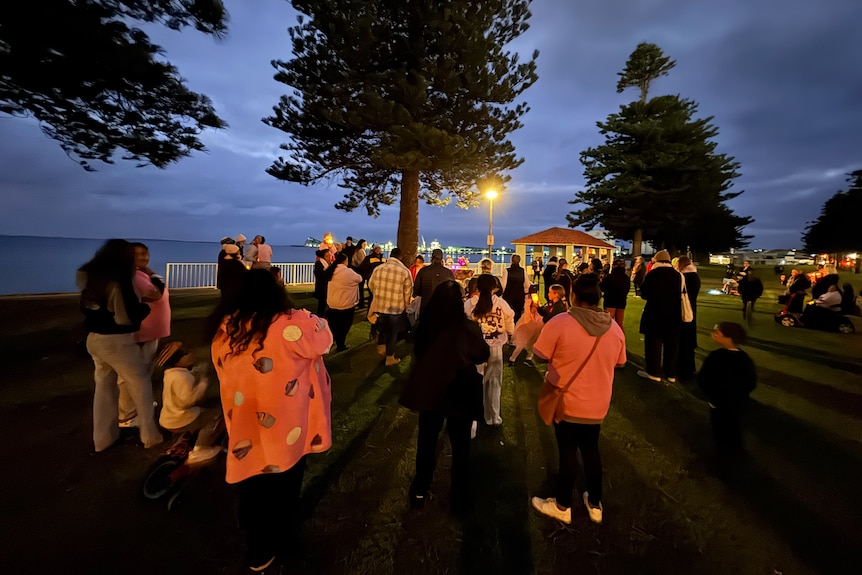 A dark night vigil, people wearing pink, ocean in the distance.