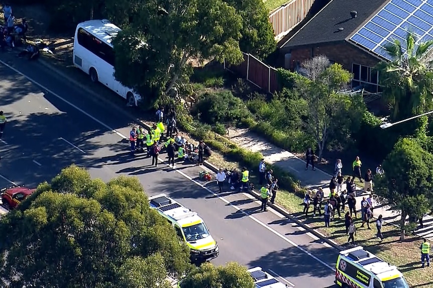 A white bus in top left with emergency serviced vehicles on the roads and people, some in hi-viz, standing around