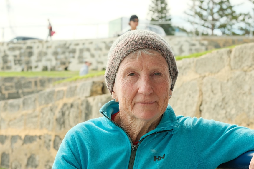 An elderly woman sits at the bench by Cottesloe Beach. 