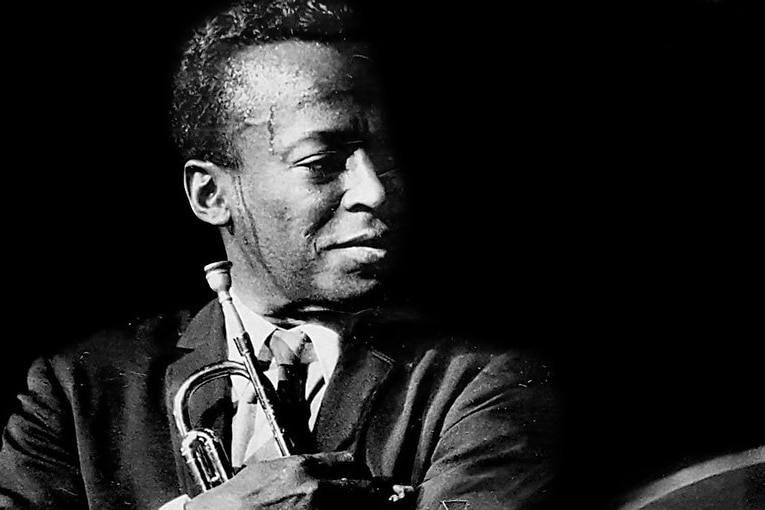 Miles Davis holding his trumpet on stage circa 1964