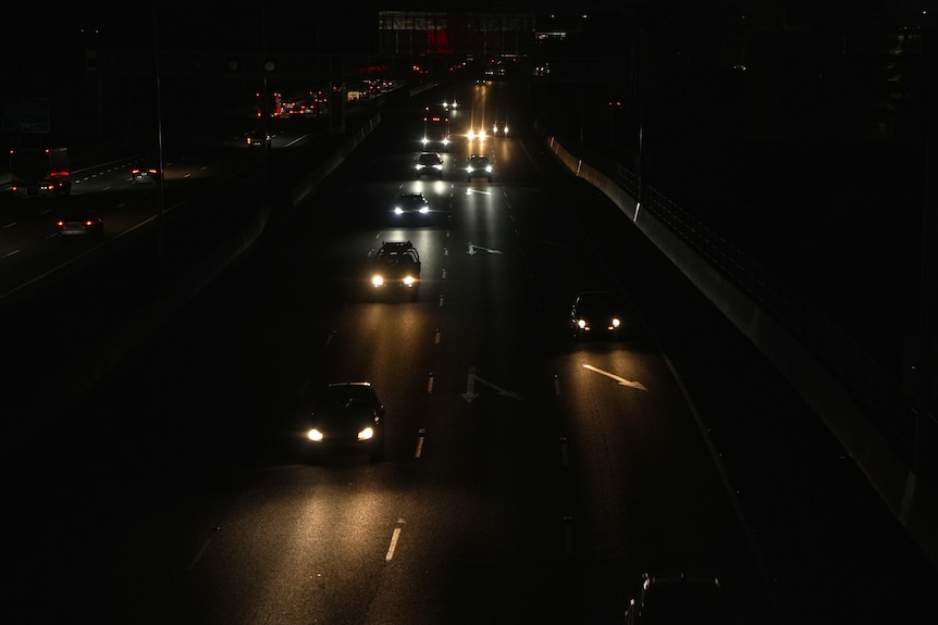 Wide shot of a highway at night time, illuminated by the headlights of cars.