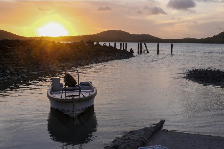 People fishing on a seawall around sunset