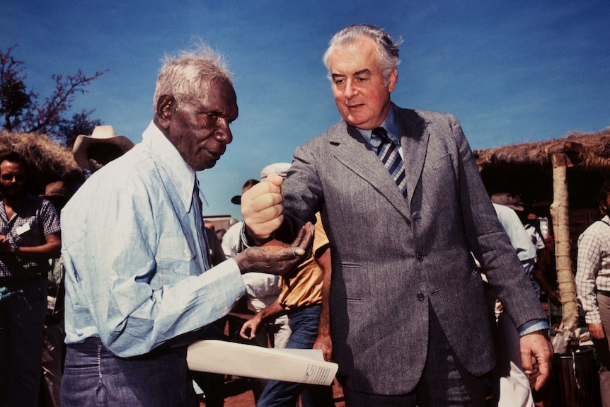 Gough Whitlam pours sand into Vincent Lingiari's hand.