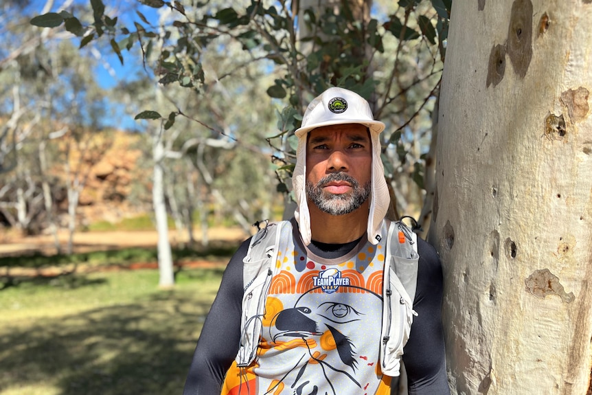 A man wearing a legionnaires cap leans against a gum tree trunk.