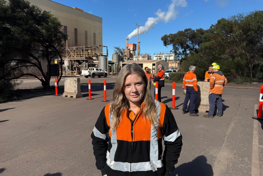 A woman wearing an orange and blue jacket at an industrial site