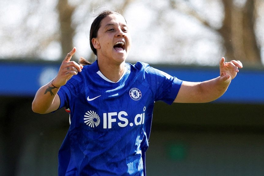 Sam Kerr celebrating on field, raising her hands up.