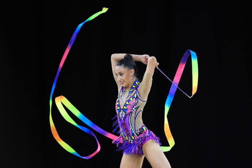 A woman holds a ribbon and smiles while twirling it in the air.