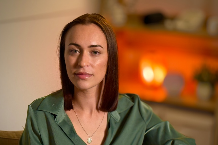 Woman with short brown hair looks at camera in a green silk shirt and in a well lit therapy room.