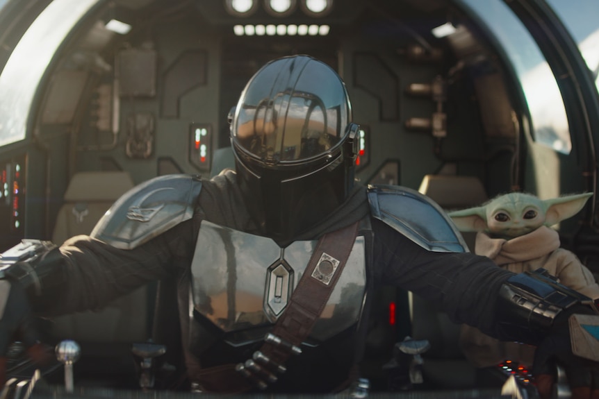 A armoured man and a small green creature sit in a spaceship