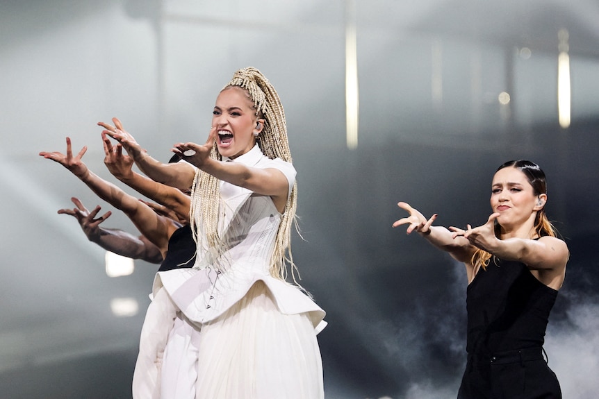 Monroe, flanked by backup dancers, sings on stage, their arms outstretched 