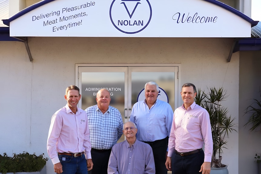 Five men outside the entry to Nolan Meats. One is seated.