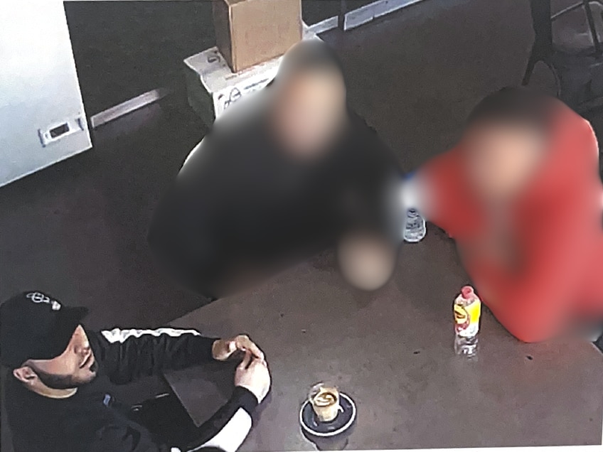 CCTV of three men, two blurred, sat at a table