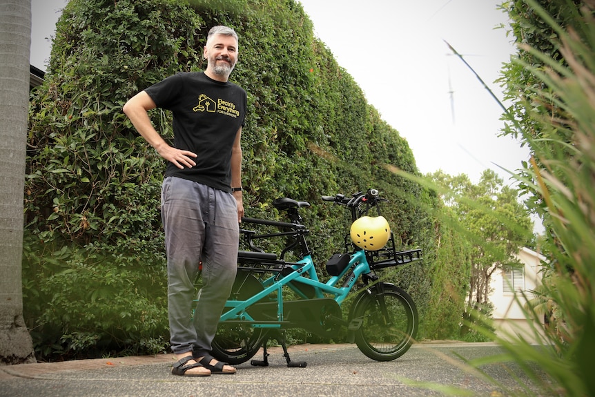 Francis stands next to a parked e-bike wearing a black t-shirt and grey long pants.