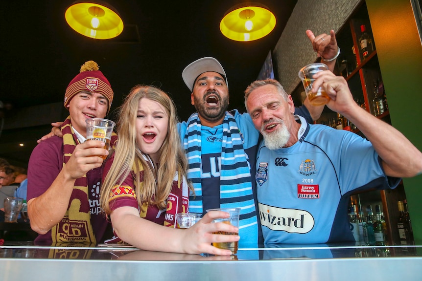 Two blues supporters and two maroons supports drinking beer and celebrating.