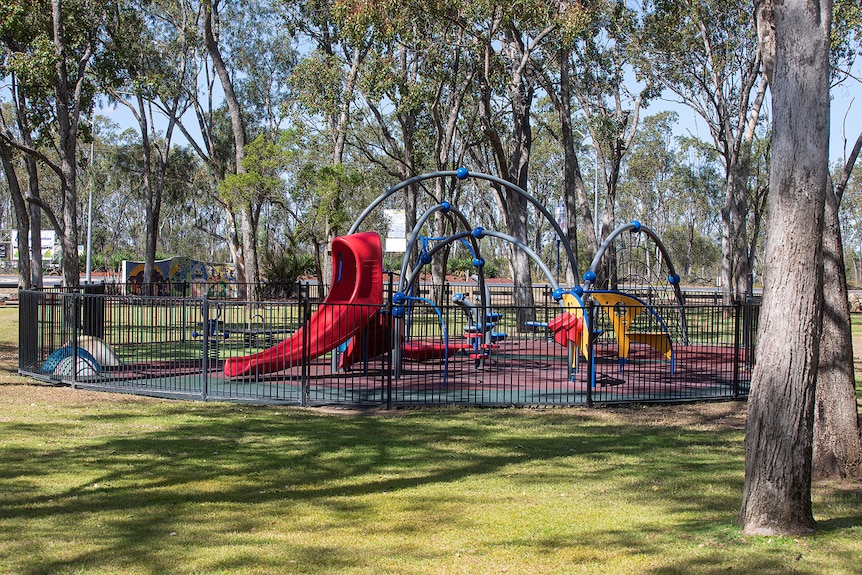 A children's playground, surrounded by large trees.