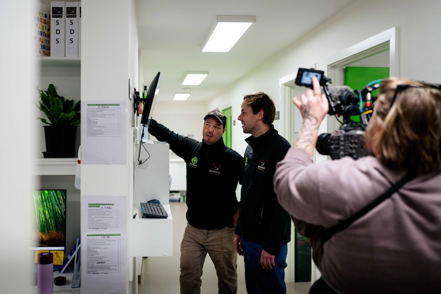 A woman holding a camera filming two men looking at an x-ray in an animal hospital