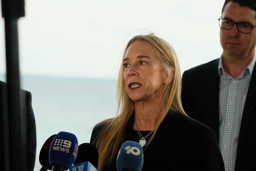 A woman with blonde hair is speaking to media. 