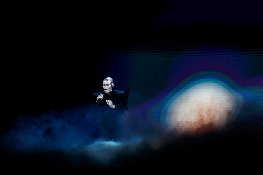 A dark image of a male singer on stage at the Eurovision Song Contest.
