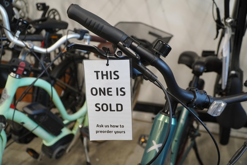A close-up shot of a white tag reading "this one is sold" on the handlebars of an electric bike in a cycle shop.
