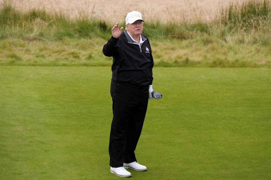 Donald Trump gestures as he starts playing golf, he is dressed in a black jumper and trousers