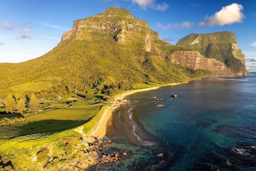 A mountainous island, taken from the air, on a sun day, with blue skies and clear water.