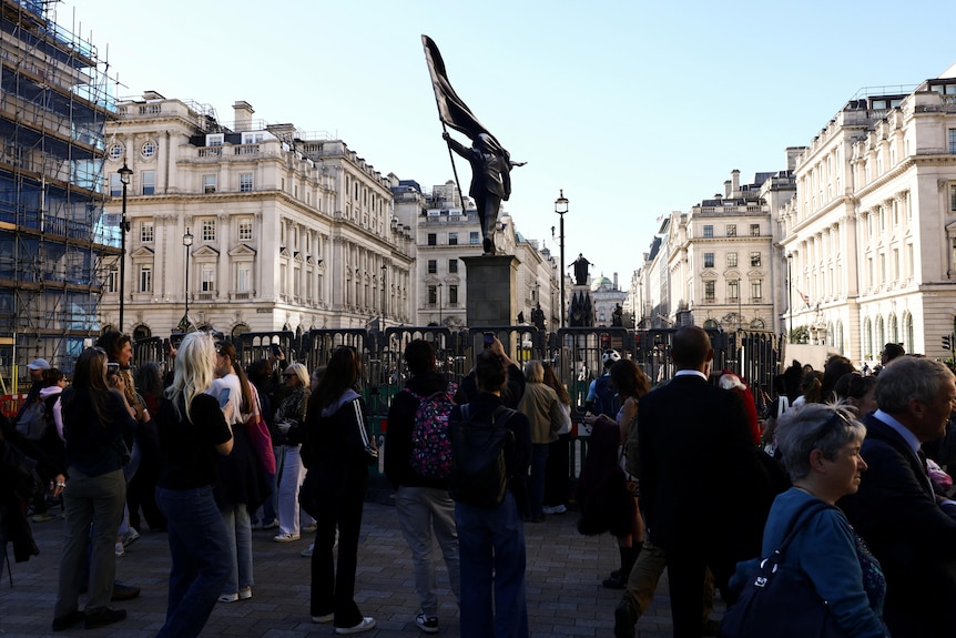 People gather next to a statue depicting a person stepping off the plinth while carrying a flag covering their face.