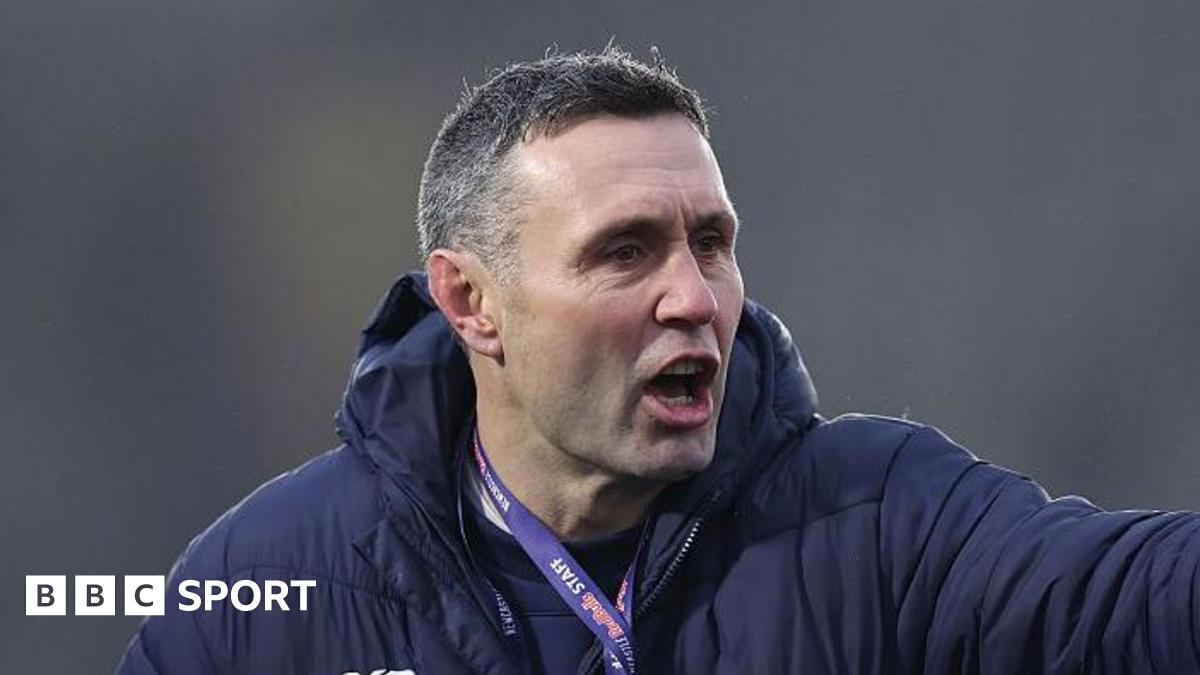 Stephen Jones pointing with his left hand towards players out of shot, while wearing a lanyard and a thick padded coat
