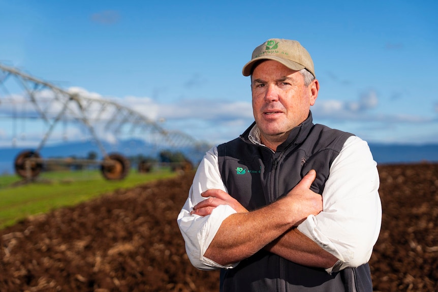 a man in a black vest with a green cap on in a field in the sun