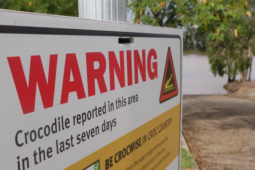 A crocodile sighting warning sign in front of a brown river.