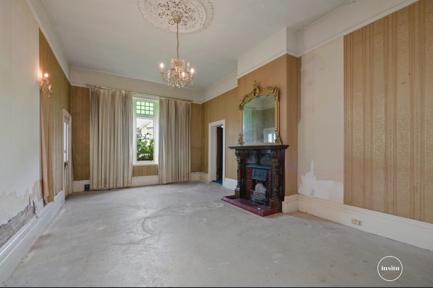 a rundown room with a fireplaces, mirror and chandelier