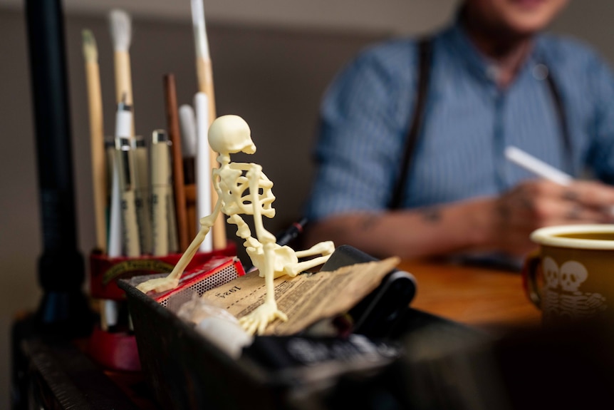 A mini skeleton figure resting in a container of art supplies in an art studio