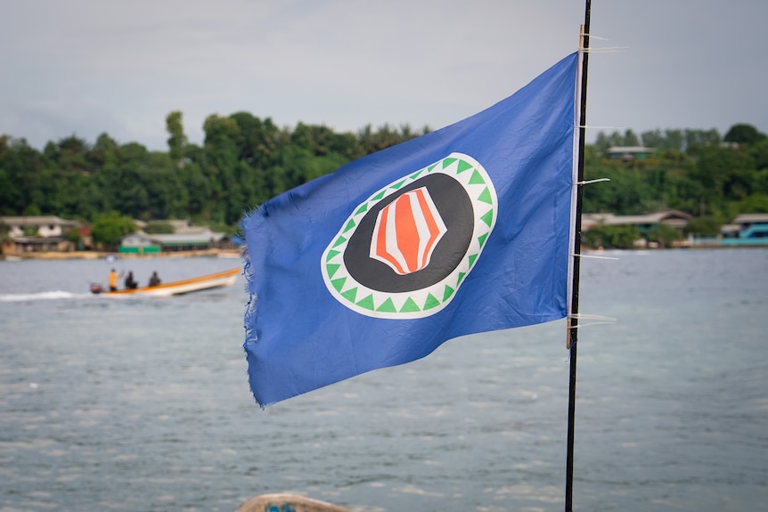 A photo of Bougainville's flag — blue with a red, black and green circle in the middle — flapping in the wind.
