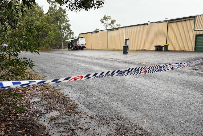 Police tape in front of a road with a yellow shed on the right.