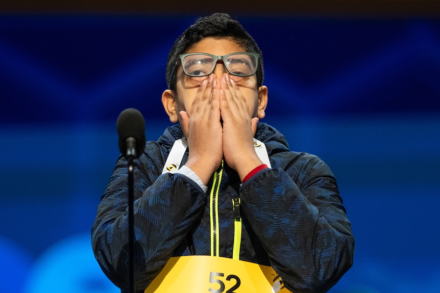 A boy with his hands on his face, pushing up his glasses