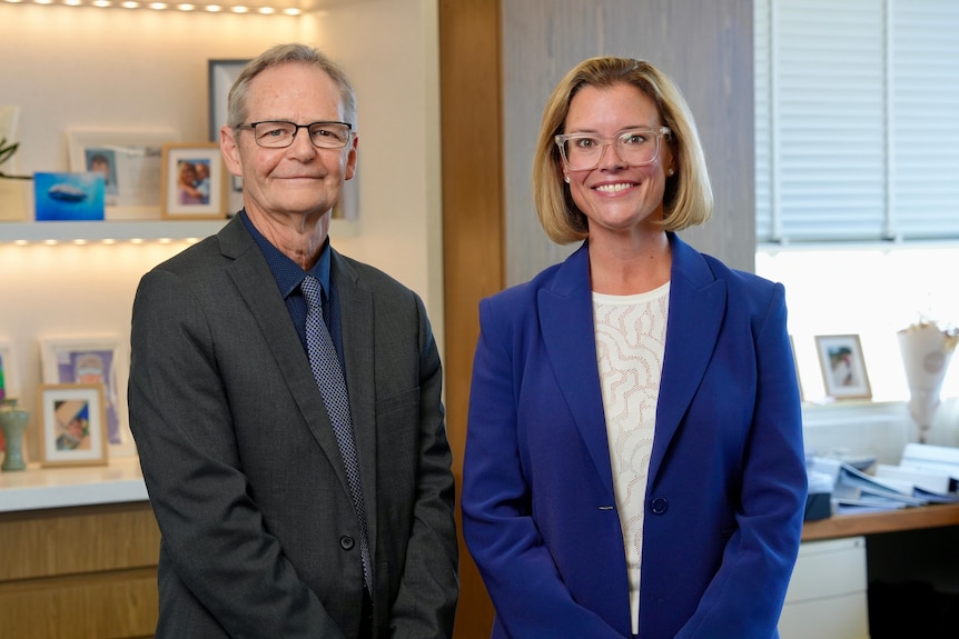 A man in dark suit and a woman in blue jacket smiling at the camera