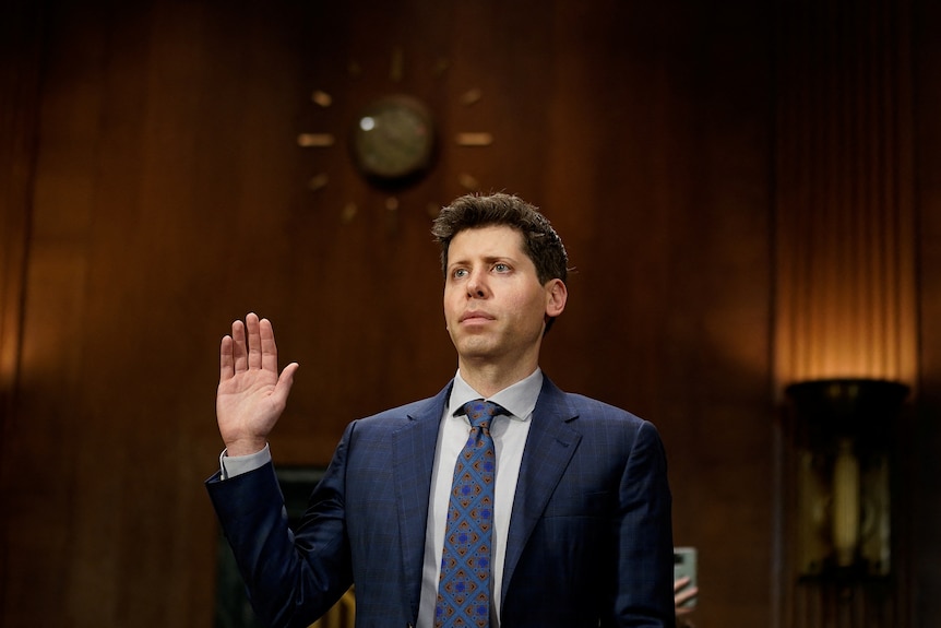 A white man in a suit holds up his hand and is sworn in.