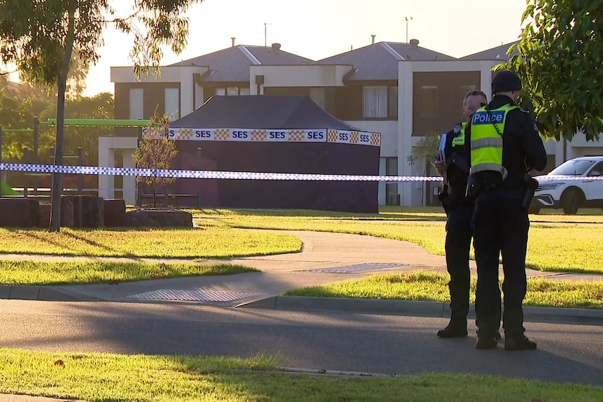 Two police officers stand near police tape that blocks off a suburban park where an SES tent stands.
