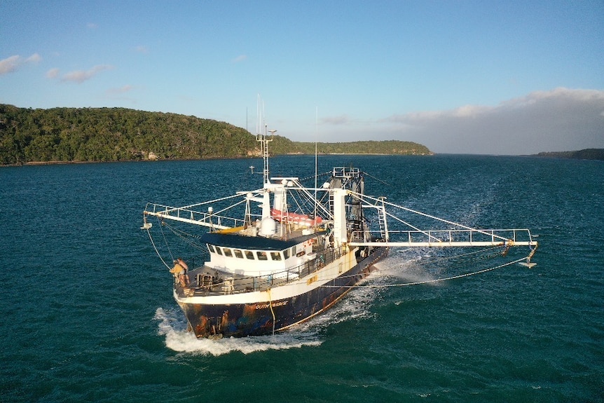 A prawn trawler out at sea with island in background.