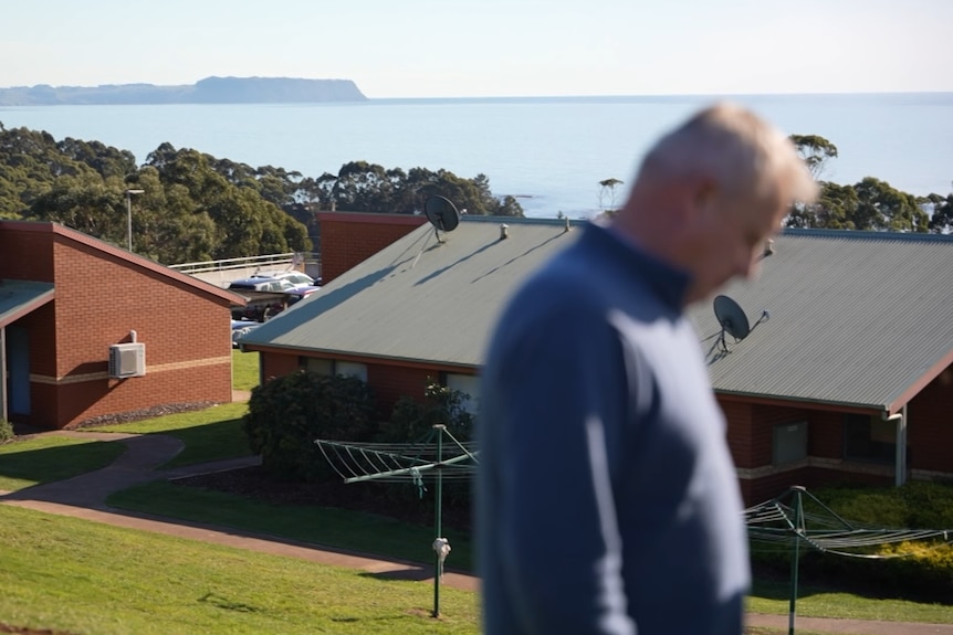 A man, out of focus, standing in front of a hospital.