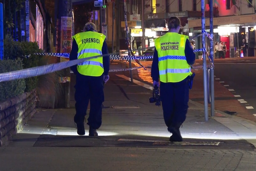 Two police officers in high-vis walking between polcie tape King Street in Newtown