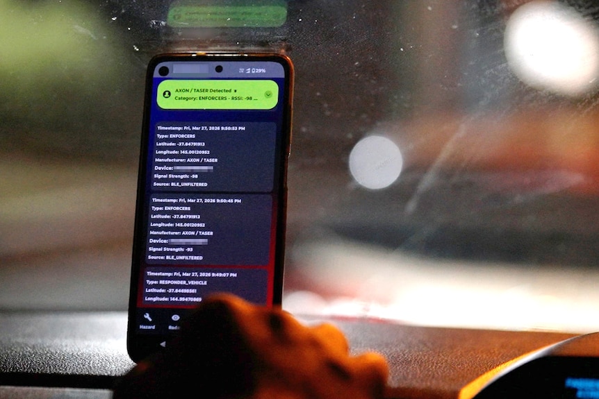A phone sitting on a car dashboard, on it is an app with details listed including longitude and latitude.