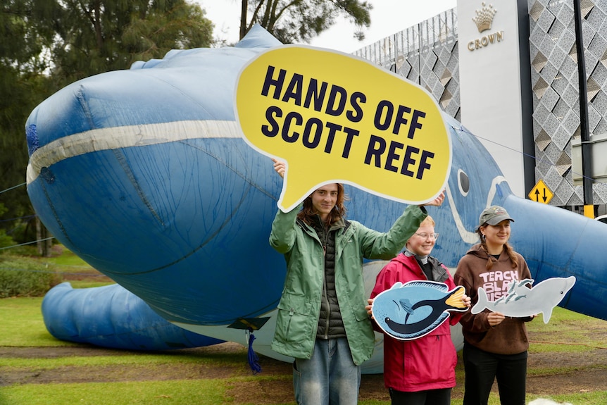 A protester hold up a sign stating 'Hands off Scott Reef' while standing in front of a giant inflatable whale